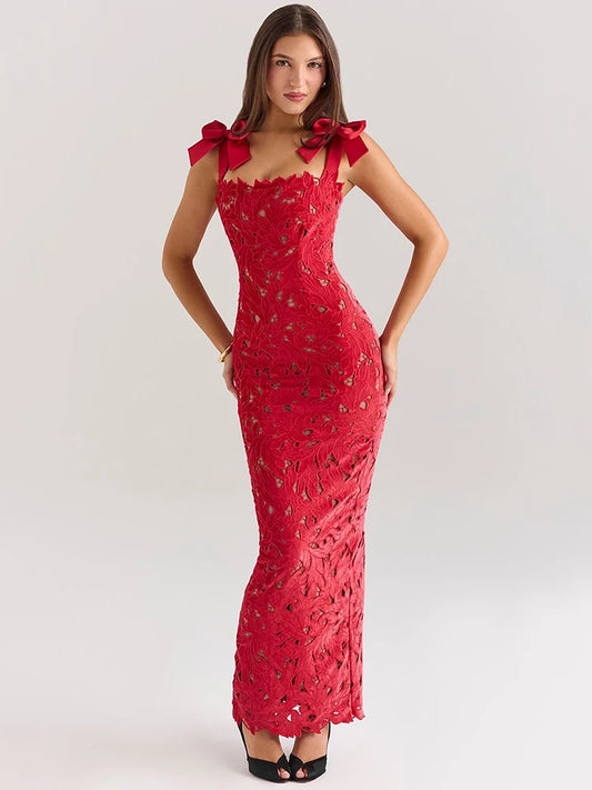 A woman wearing a red lace maxi dress with a fitted silhouette, bow-embellished straps, and a subtle back slit.