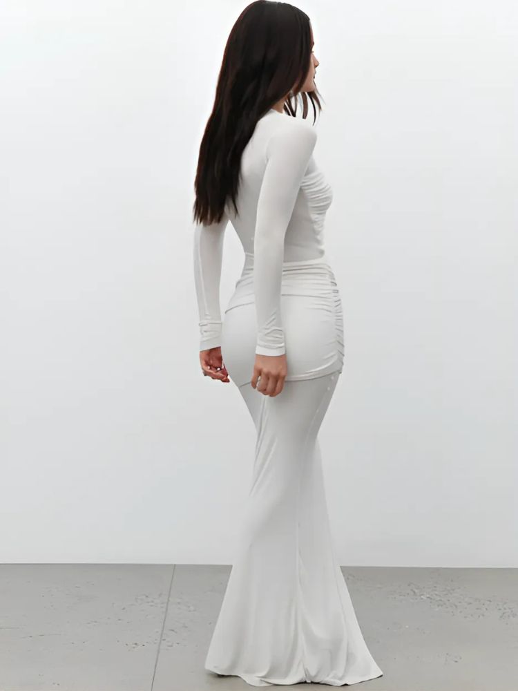 A woman wearing a white long-sleeved bodycon maxi dress with diagonal ruched details on the chest and hip, featuring a fitted silhouette and a flowy hem from the knee down.