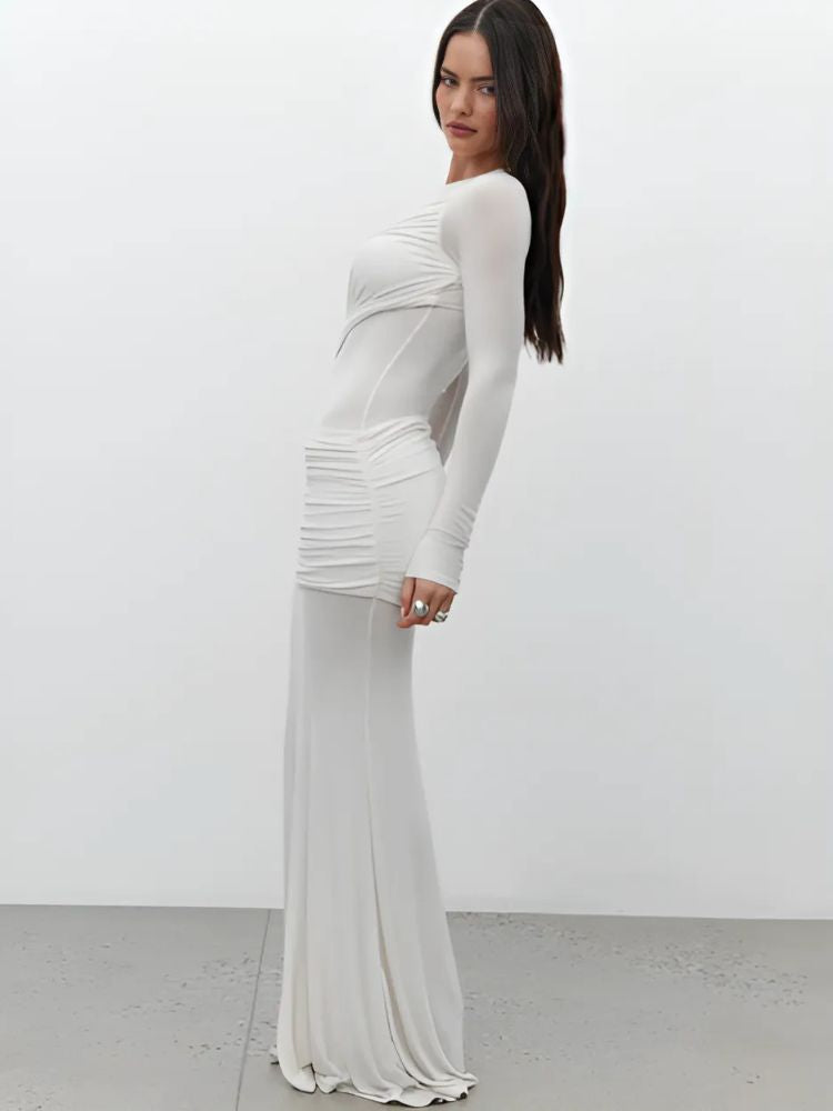 A woman wearing a white long-sleeved bodycon maxi dress with diagonal ruched details on the chest and hip, featuring a fitted silhouette and a flowy hem from the knee down.