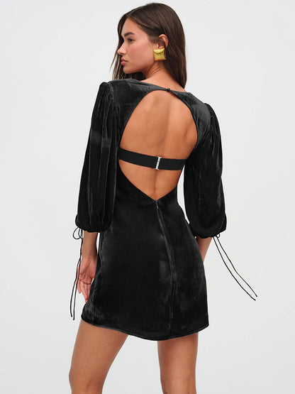 Woman wearng a black velvet mini dress. The dress features a structured bust, long billowy sleeves with adjustable ties, and an open back with a clasp.