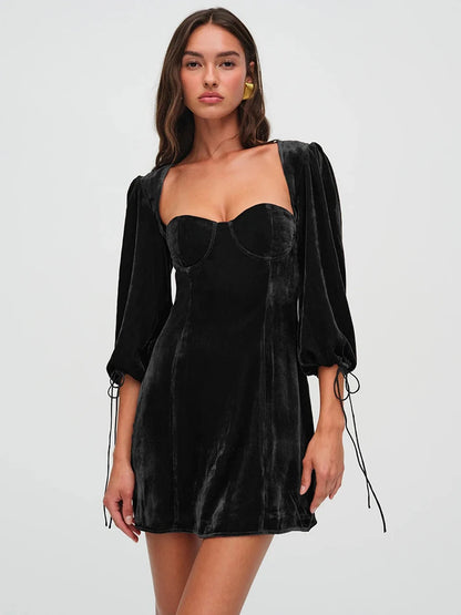 Woman wearng a black velvet mini dress. The dress features a structured bust, long billowy sleeves with adjustable ties, and an open back with a clasp.