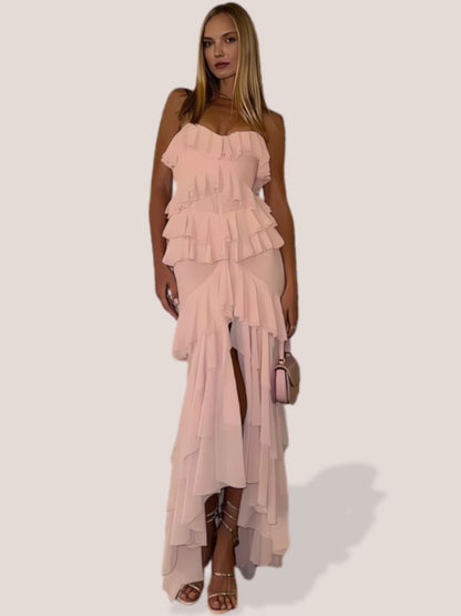 Woman wearing a light pink Maxi Dress, showcasing the strapless design, tiered ruffles, and a thigh-high slit.