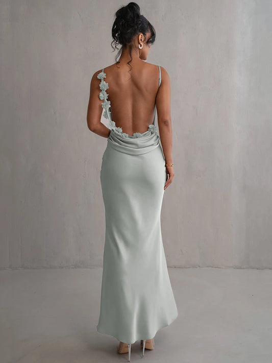 Light green satin ankle-length maxi dress with slight stretch, V-neckline, spaghetti straps, and a backless design. Features a flower decoration at the back, with a pullover closure.