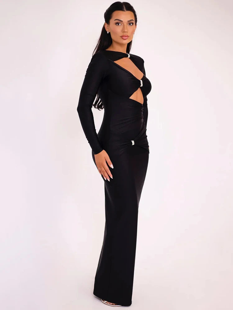 Woman wearing a black long sleeve maxi dress with hollow-out details and sparkling brooch accents at the neck, bust, and waist.