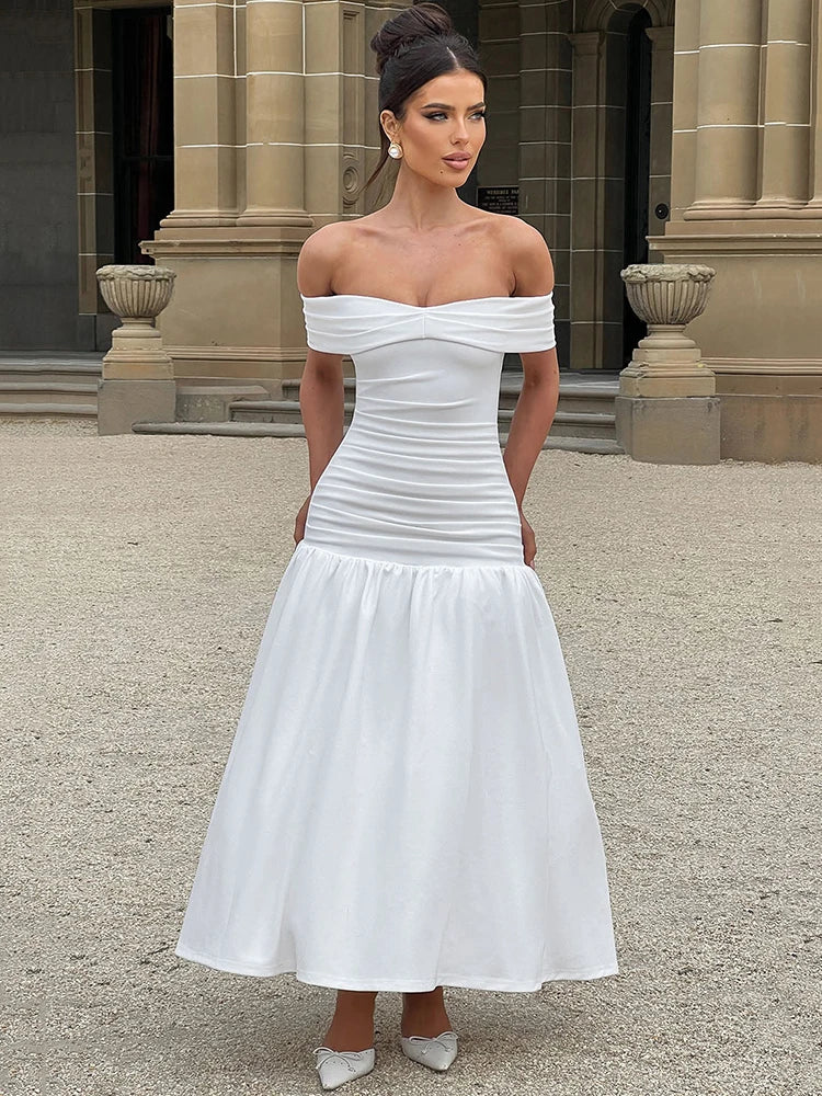 Woman wearing a white midaxi dress with a dropped waist, full gathered skirt, and pleated Bardot neckline, showcasing an elegant off-shoulder design