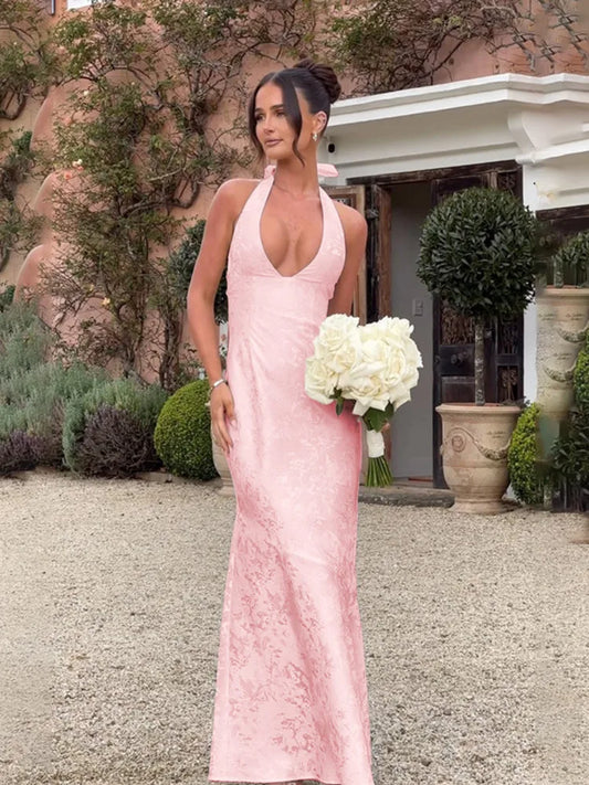 Woman wearing a pink satin maxi dress with a deep V-neck, lace-up back, sleeveless, backless design, mermaid silhouette and floor-length