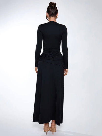 Woman wearing a black long-sleeved maxi dress with deep V-neck, thigh-high split, and ruched knot detailing