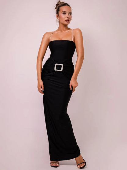 A woman wearing a black sleek, backless maxi dress with glittering spaghetti straps and a glitter-decorated hip buckle.