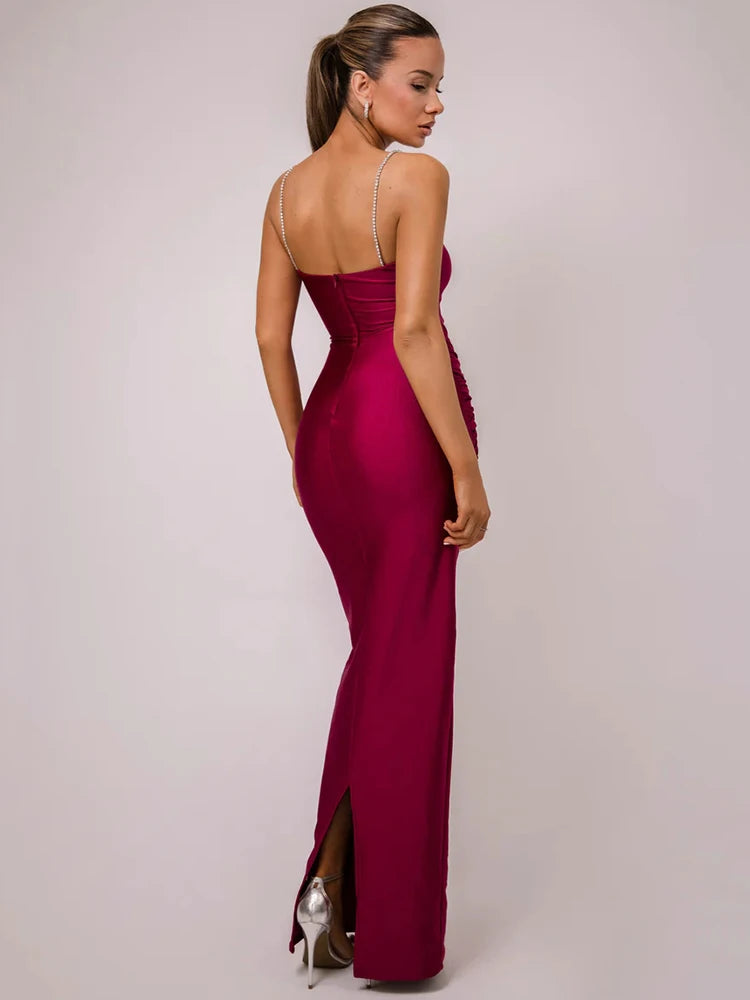 A woman wearing a pink sleek, backless maxi dress with glittering spaghetti straps and a glitter-decorated hip buckle.