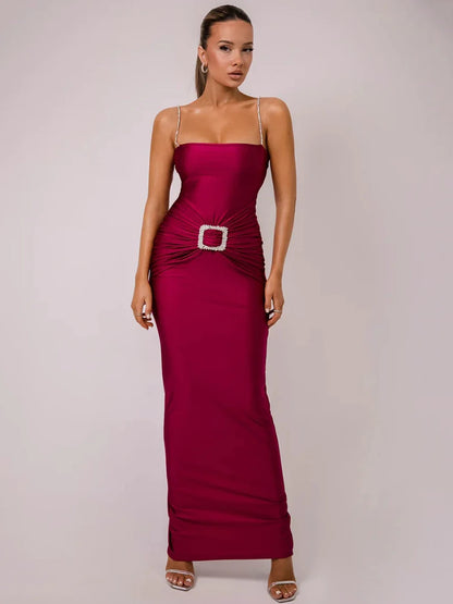 A woman wearing a pink sleek, backless maxi dress with glittering spaghetti straps and a glitter-decorated hip buckle.