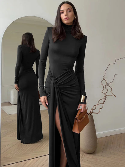 Woman wearing a black maxi dress  with a turtleneck, thigh-high split, long sleeves, draped hips and a bodycon fit