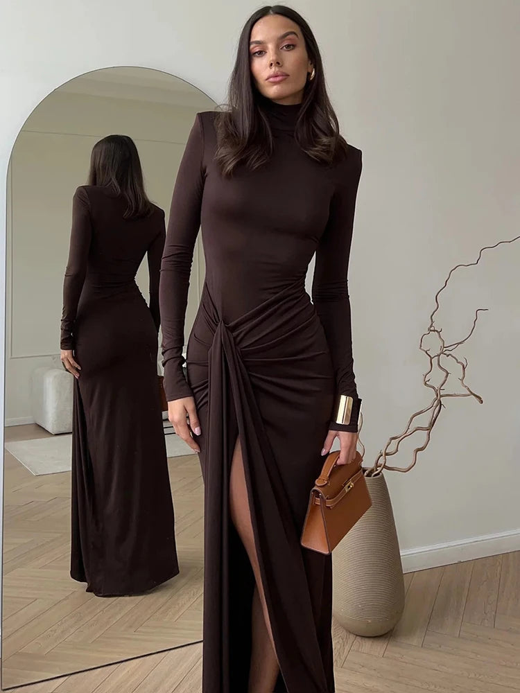 Woman wearing a brown maxi dress  with a turtleneck, thigh-high split, long sleeves, draped hips and a bodycon fit