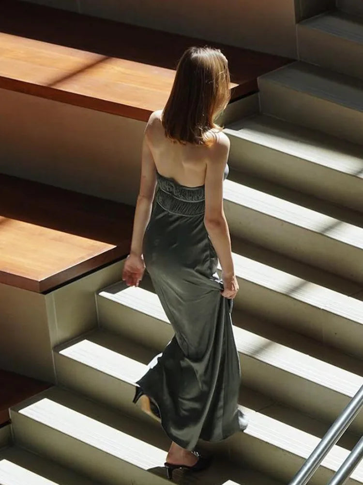 Woman wearing a silver Maxi Dress in satin with a deep V-neckline, draped halter, backless bodycon style and sleeveless.