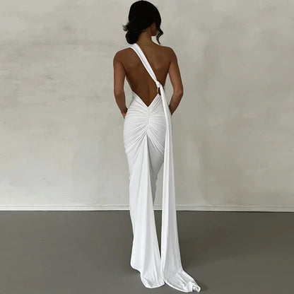 White bodycon maxi dress with a backless design, oblique shoulder, ruched detailing, and strap accents. Features a trumpet/mermaid silhouette, strapless neckline, and off-the-shoulder sleeves.