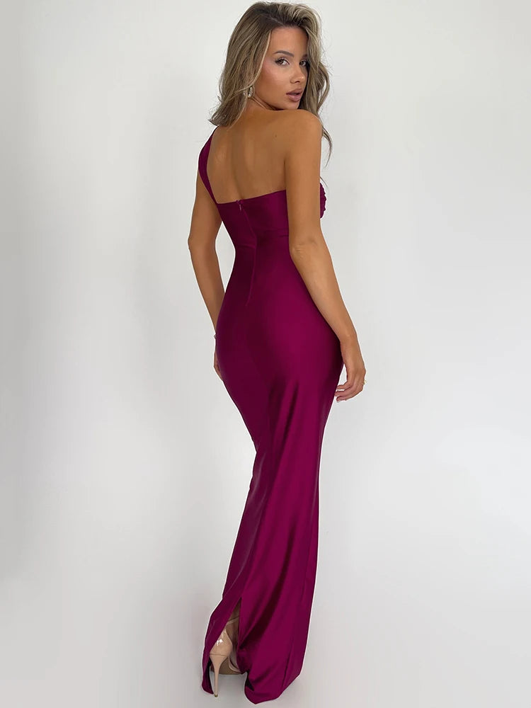 A woman wearing a pink bodycon maxi dress with a one-shoulder design, strapless and backless style, and intricate draping. The dress accentuates her figure, offering a sleek and elegant look, perfect for special occasions