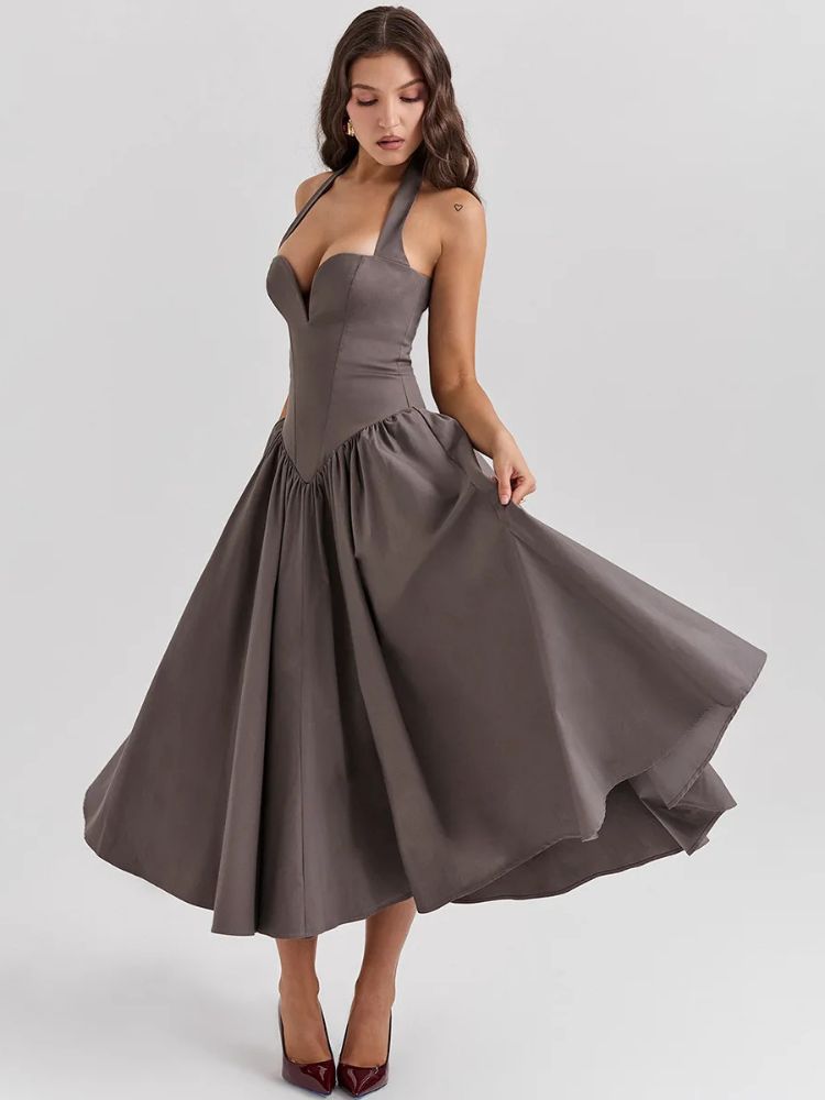 Woman wearing a khaki gray midaxi dress with a deep halter v neck, pleated skirt an neck mounted backless design.