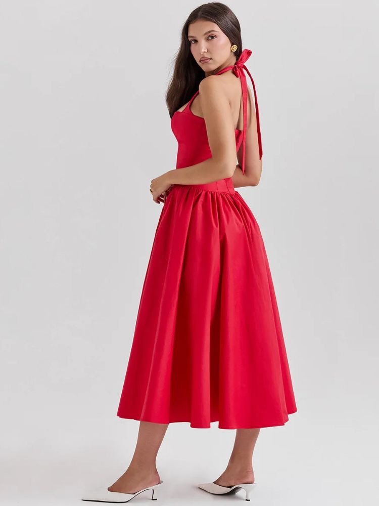 Woman wearing a red midaxi dress with a deep halter v neck, pleated skirt an neck mounted backless design.