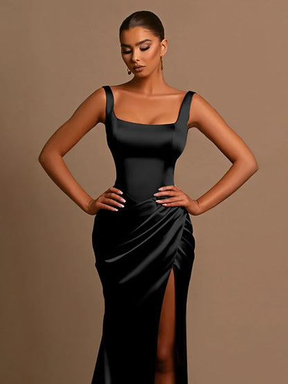 Woman wearing a black Maxi Dress in stretchy satin with a square neckline, thigh-high split, backless style, ruched hips, and tank straps.