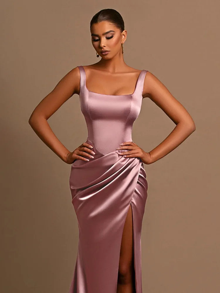 Woman wearing a pink Maxi Dress in stretchy satin with a square neckline, thigh-high split, backless style, ruched hips, and tank straps.