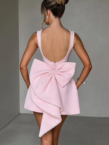 Woman wearing a pink backless mini dress with pearl bow detail and pearl-embellished collar, sleeveless high-waist A-line silhouette.